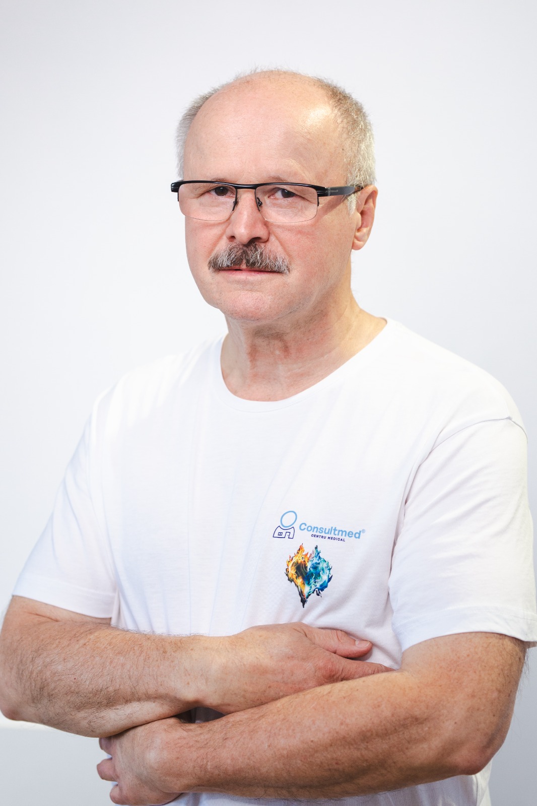 Portrait of a middle-aged man with glasses and a mustache, wearing a white t-shirt with a blue logo, arms crossed.